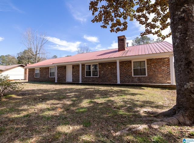 back of property with a yard, metal roof, brick siding, and a chimney