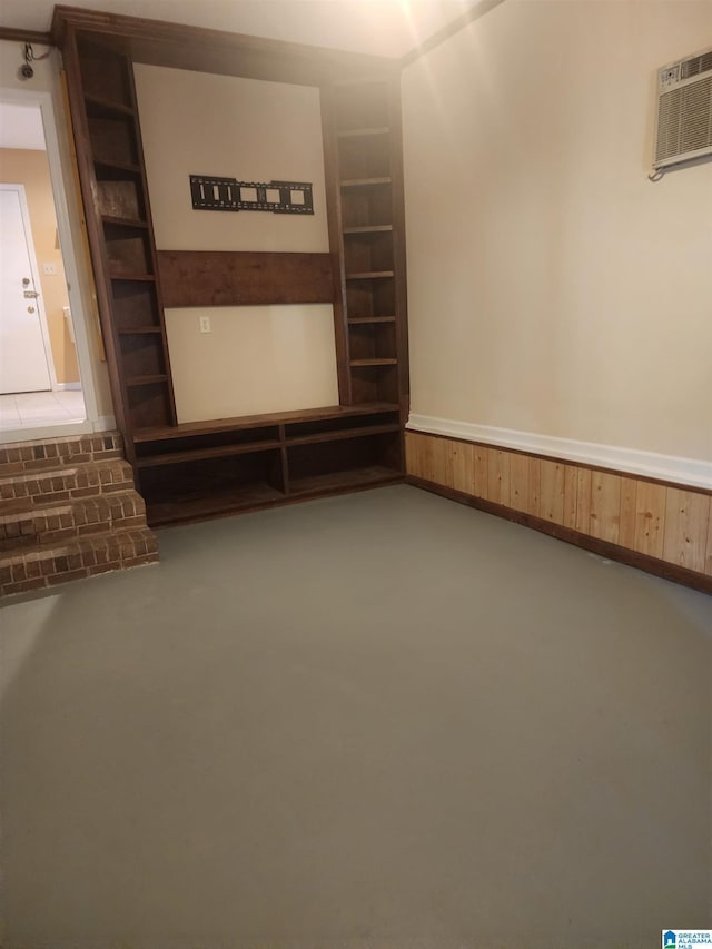 interior space featuring built in features, an AC wall unit, a wainscoted wall, and concrete floors