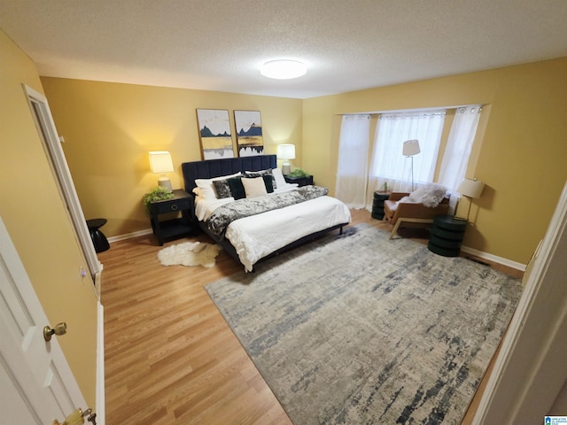 bedroom featuring baseboards, wood finished floors, and a textured ceiling