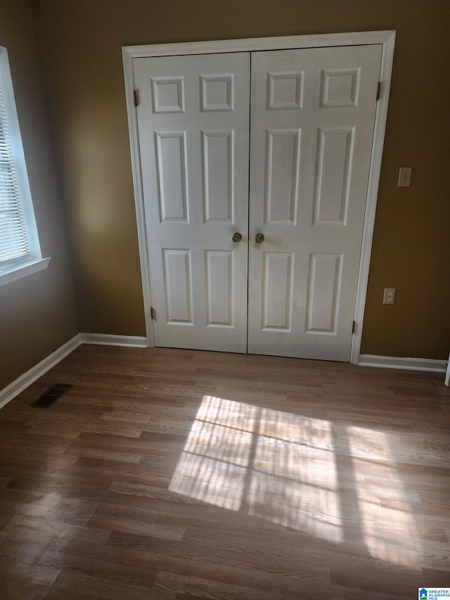 unfurnished bedroom with baseboards, a closet, visible vents, and wood finished floors