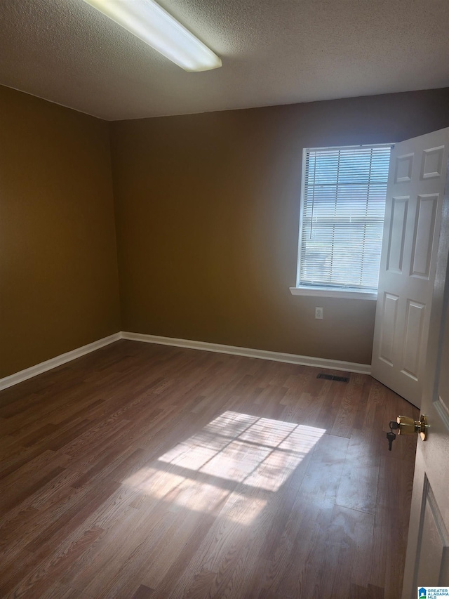 spare room featuring visible vents, a textured ceiling, baseboards, and wood finished floors