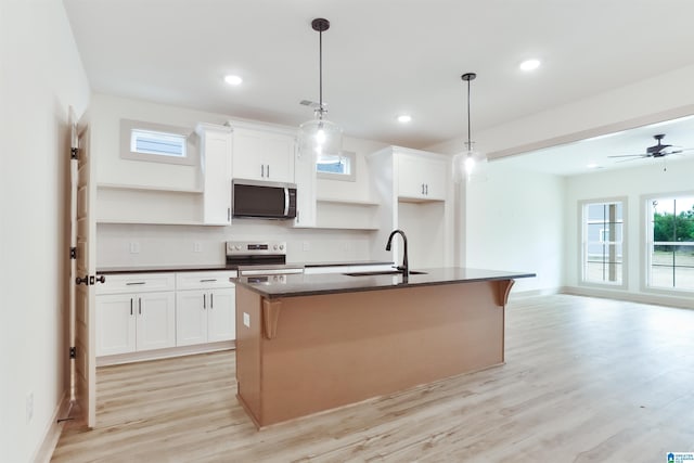 kitchen featuring a kitchen island with sink, a sink, white cabinetry, appliances with stainless steel finishes, and dark countertops