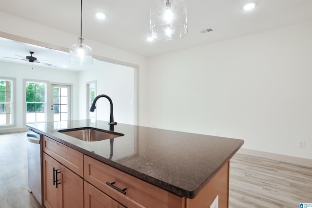 kitchen with visible vents, dark stone counters, a kitchen island with sink, pendant lighting, and a sink