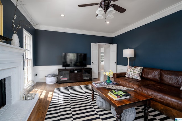 living room with a wainscoted wall, a brick fireplace, ornamental molding, and wood finished floors