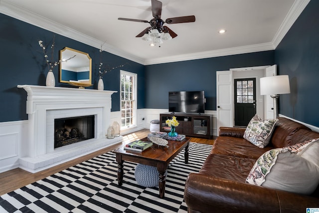 living area featuring a wainscoted wall, a brick fireplace, ornamental molding, and wood finished floors