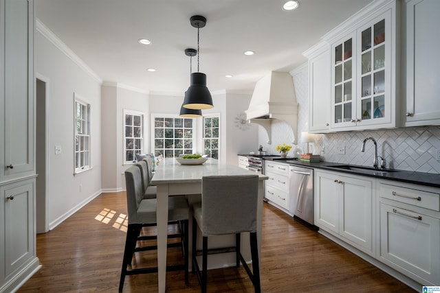 kitchen with dishwasher, custom range hood, dark wood-type flooring, a sink, and backsplash