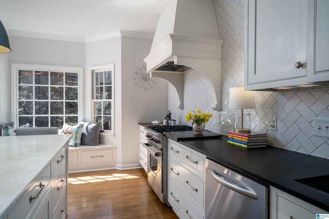 kitchen featuring wood finished floors, stainless steel appliances, crown molding, premium range hood, and backsplash