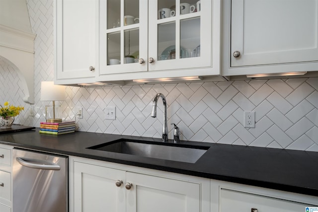 kitchen with a sink, white cabinets, dishwasher, dark countertops, and glass insert cabinets