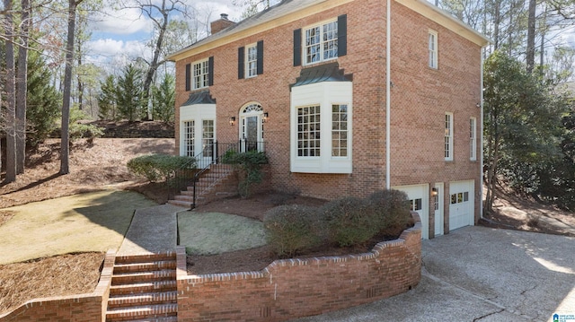 view of front of property with driveway, a garage, a chimney, stairway, and brick siding