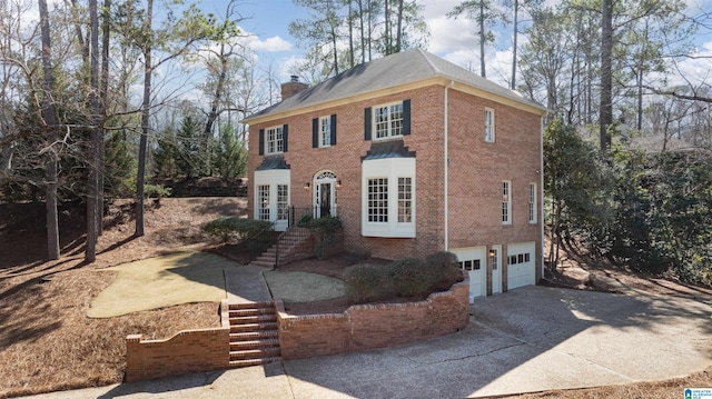 view of front of home featuring a garage, brick siding, concrete driveway, french doors, and a chimney