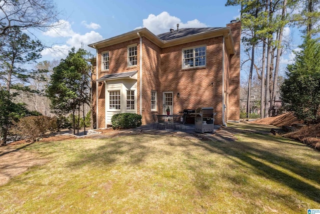 back of house featuring a patio, a chimney, a lawn, and brick siding