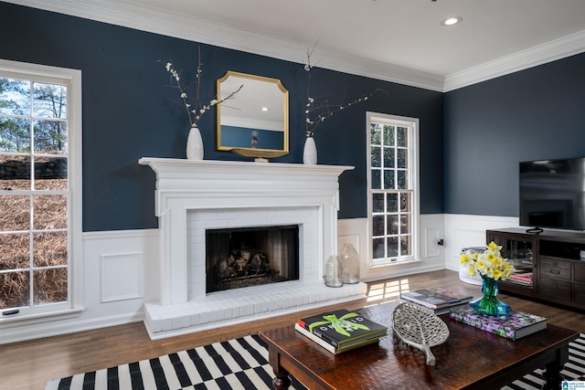 living room with ornamental molding, a brick fireplace, wood finished floors, and a wealth of natural light