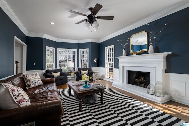 living area with a brick fireplace, wainscoting, wood finished floors, and crown molding