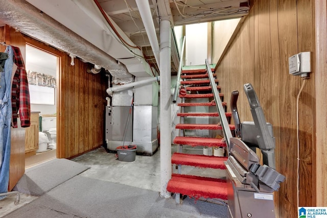 unfinished basement featuring stairway, heating unit, and wooden walls