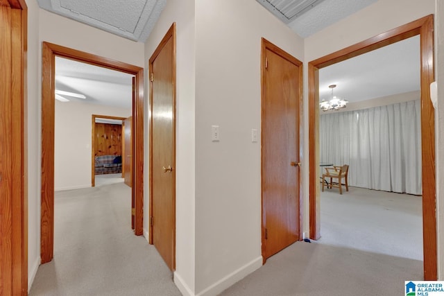 corridor with light colored carpet, baseboards, and an inviting chandelier