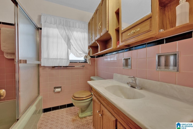 bathroom with toilet, bath / shower combo with glass door, vanity, and tile walls