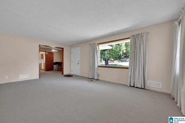 unfurnished room with visible vents, a chandelier, a textured ceiling, and light colored carpet