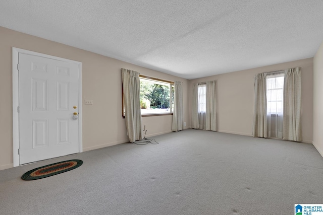 interior space featuring a textured ceiling, baseboards, and light colored carpet