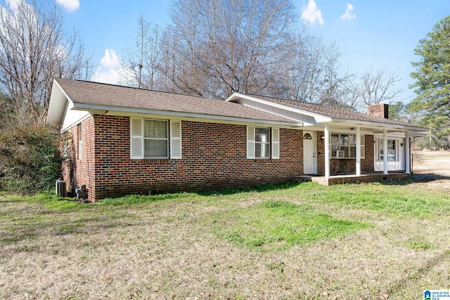 ranch-style house featuring brick siding, a shingled roof, a chimney, covered porch, and a front yard