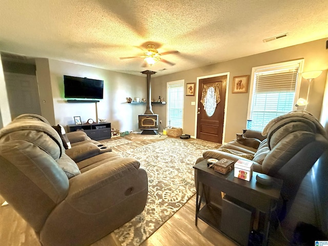 living area with light wood-style floors, a wealth of natural light, a wood stove, and visible vents