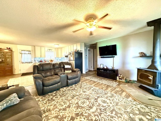 living room with a textured ceiling, light wood finished floors, a wood stove, and a ceiling fan