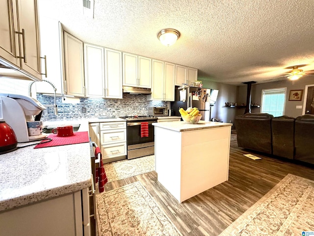 kitchen with a center island, stainless steel appliances, a wood stove, open floor plan, and under cabinet range hood