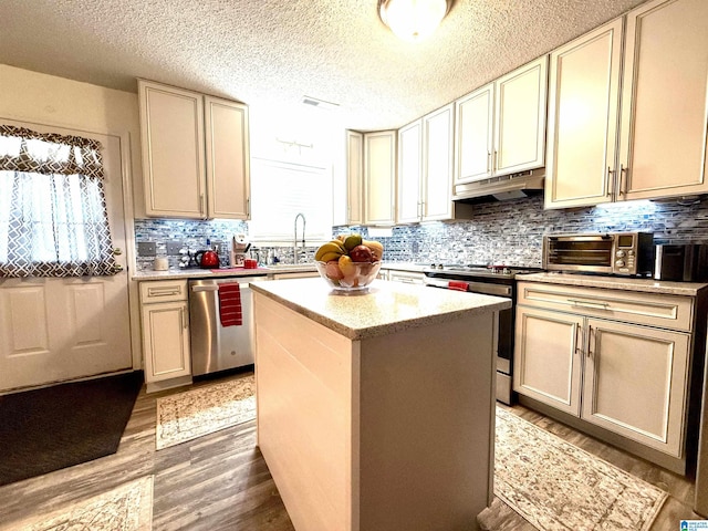 kitchen with cream cabinets, under cabinet range hood, light countertops, appliances with stainless steel finishes, and a center island