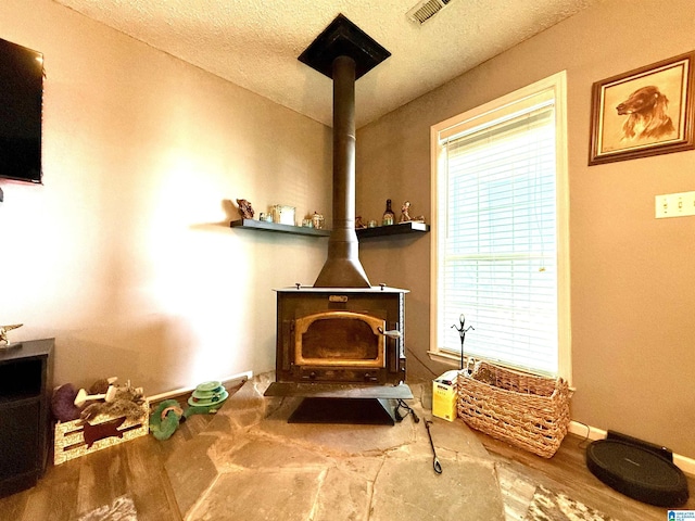 room details with baseboards, visible vents, wood finished floors, a wood stove, and a textured ceiling