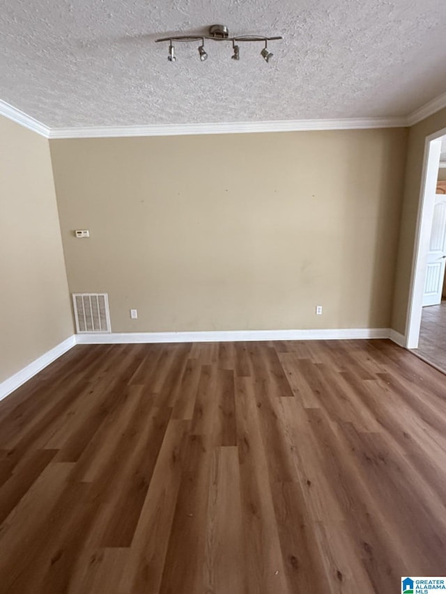 empty room with visible vents, ornamental molding, a textured ceiling, wood finished floors, and baseboards