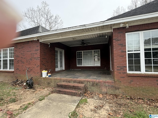 view of exterior entry with a ceiling fan, brick siding, and a patio