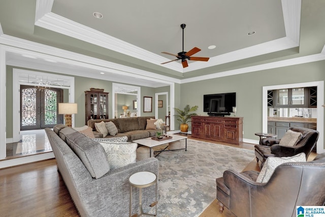 living room featuring ornamental molding, a tray ceiling, french doors, and wood finished floors