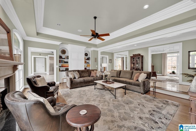 living area featuring a raised ceiling, a ceiling fan, wood finished floors, crown molding, and a high end fireplace