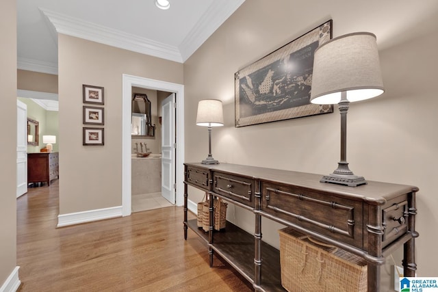 corridor featuring light wood-style flooring, ornamental molding, and baseboards