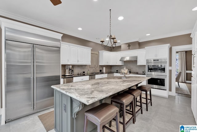 kitchen with under cabinet range hood, appliances with stainless steel finishes, backsplash, and a center island