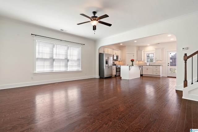 unfurnished living room with arched walkways, visible vents, stairway, dark wood-type flooring, and a sink