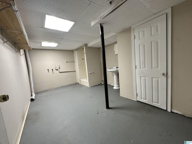 finished basement with a paneled ceiling, baseboards, and a sink