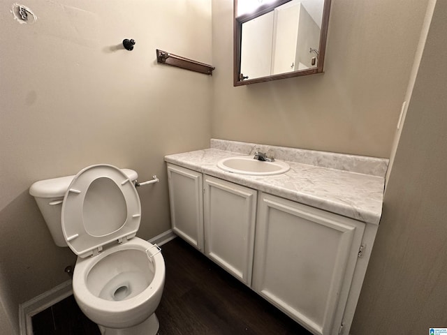 half bath with toilet, baseboards, wood finished floors, and vanity