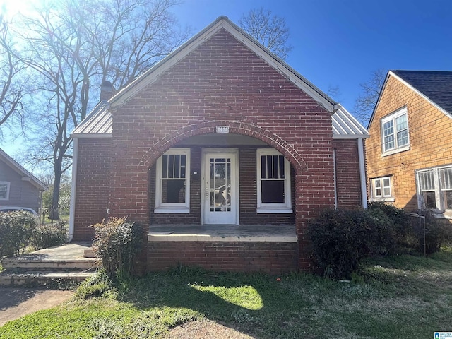 view of front of home with a chimney, metal roof, and brick siding