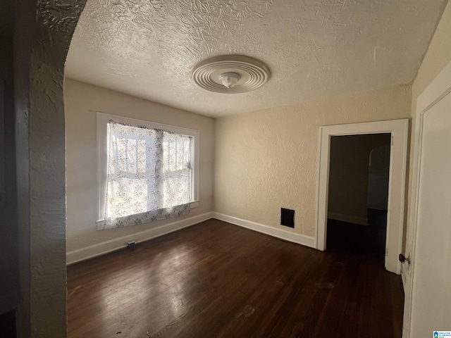 unfurnished room featuring dark wood-style floors, baseboards, a textured ceiling, and a textured wall