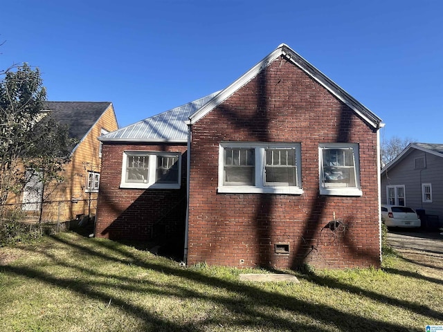 view of home's exterior with metal roof, a yard, brick siding, and fence