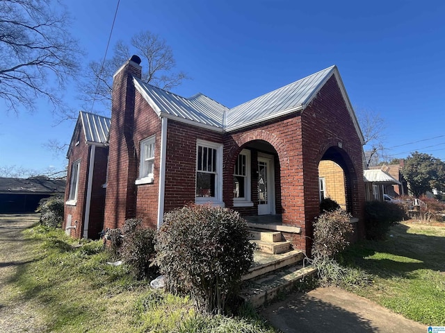 view of front of house featuring metal roof, brick siding, a chimney, and a front lawn