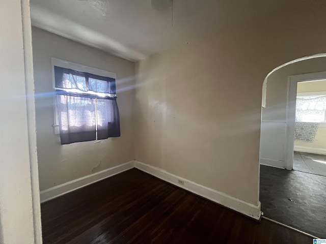 empty room featuring arched walkways, dark wood-style flooring, and baseboards