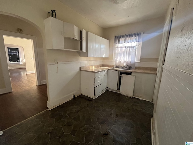 kitchen with arched walkways, open shelves, light countertops, white cabinets, and a sink