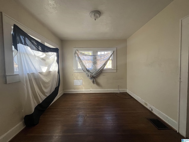 spare room featuring dark wood-style flooring, visible vents, and baseboards