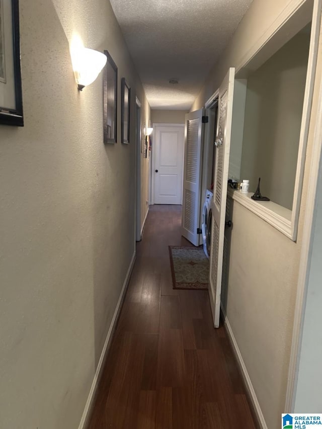 hall featuring washer / clothes dryer, dark wood finished floors, a textured ceiling, and baseboards