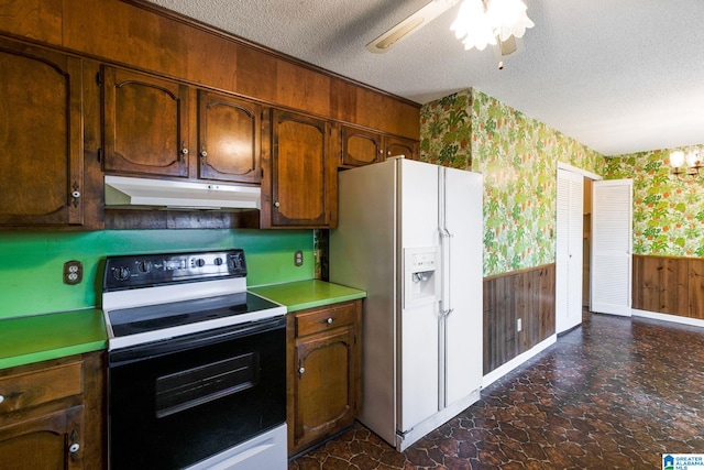 kitchen with under cabinet range hood, a wainscoted wall, range with electric stovetop, white fridge with ice dispenser, and wallpapered walls