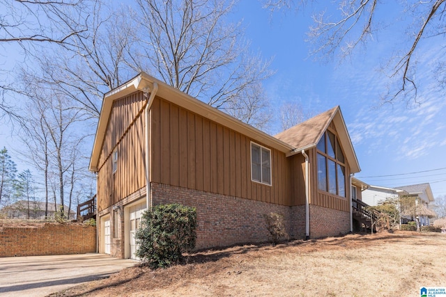 view of property exterior with driveway, brick siding, board and batten siding, and an attached garage