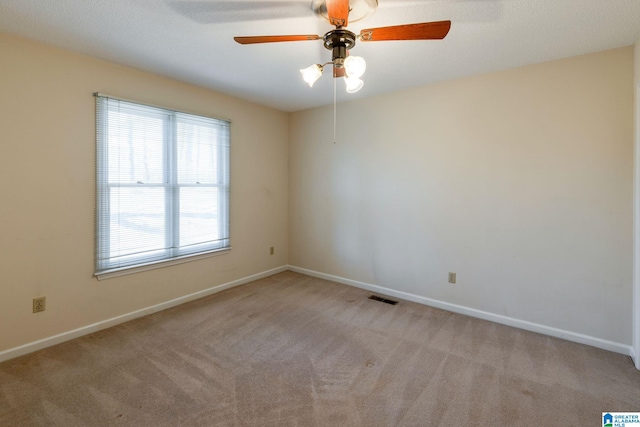 empty room featuring a ceiling fan, light colored carpet, visible vents, and baseboards