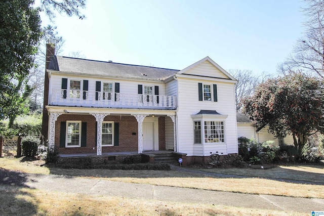 view of front of home with covered porch, brick siding, a chimney, and a balcony