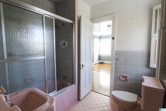 full bath with toilet, bath / shower combo with glass door, a sink, tile walls, and tile patterned floors